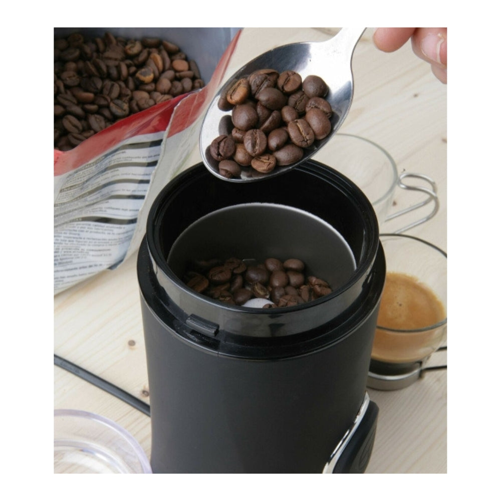 Coffee beans being scooped into a Black Decker coffee grinder, with a bag of beans and a cup of coffee in the background